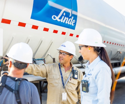 Three Linde employees in hard hats talking beside a Linde branded bulk gas delivery vehicle.