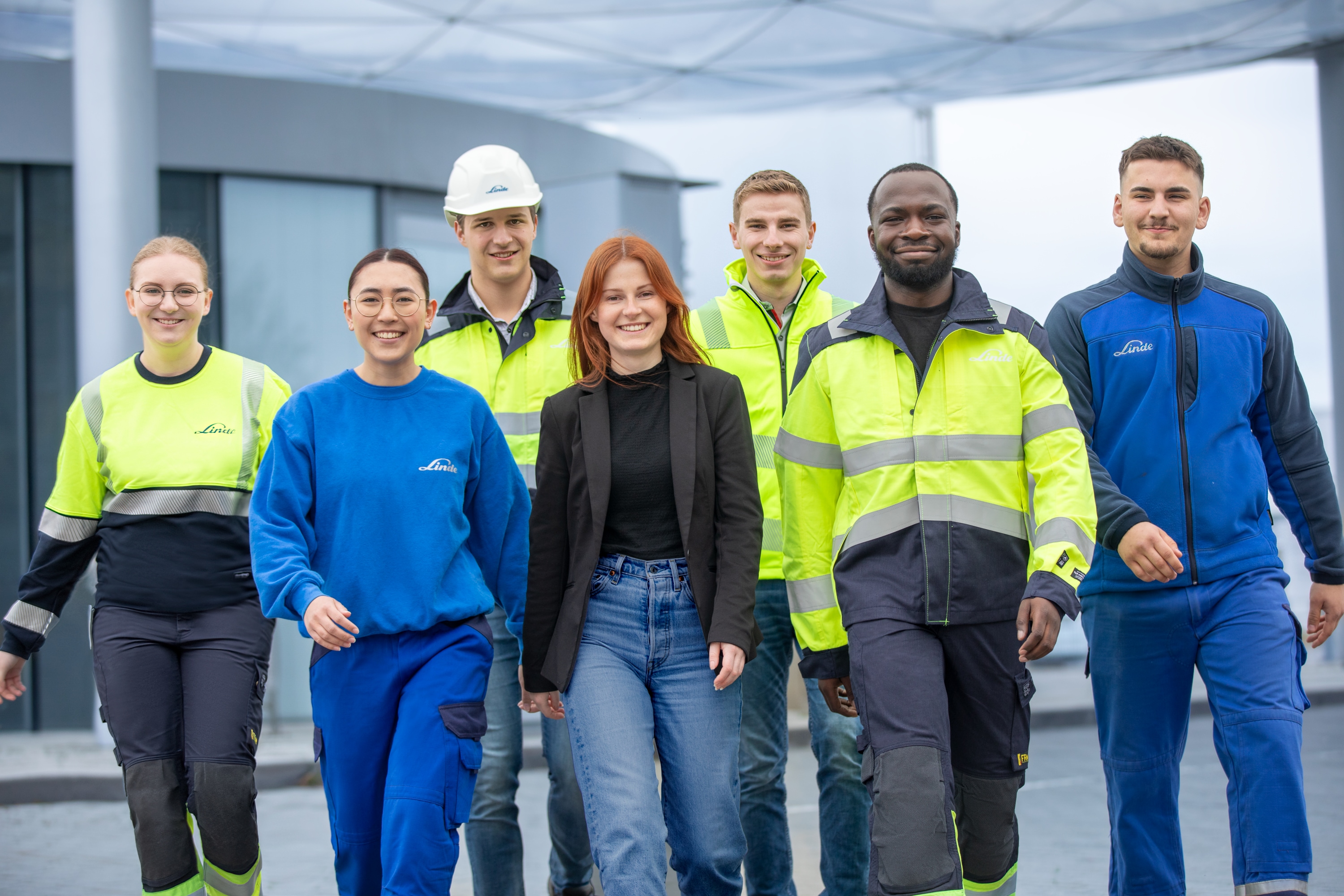 "Group picture of Linde Apprentices and Students in work gear at the hydrogen filling station walking toward the camera."