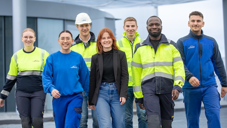"Group picture of Linde Apprentices and Students in work gear at the hydrogen filling station walking toward the camera."