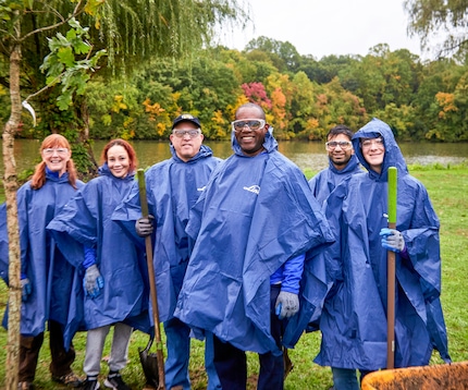 "Group photo of Linde employees outside in the rain in blue branded raincoats while volunteering and planting trees."