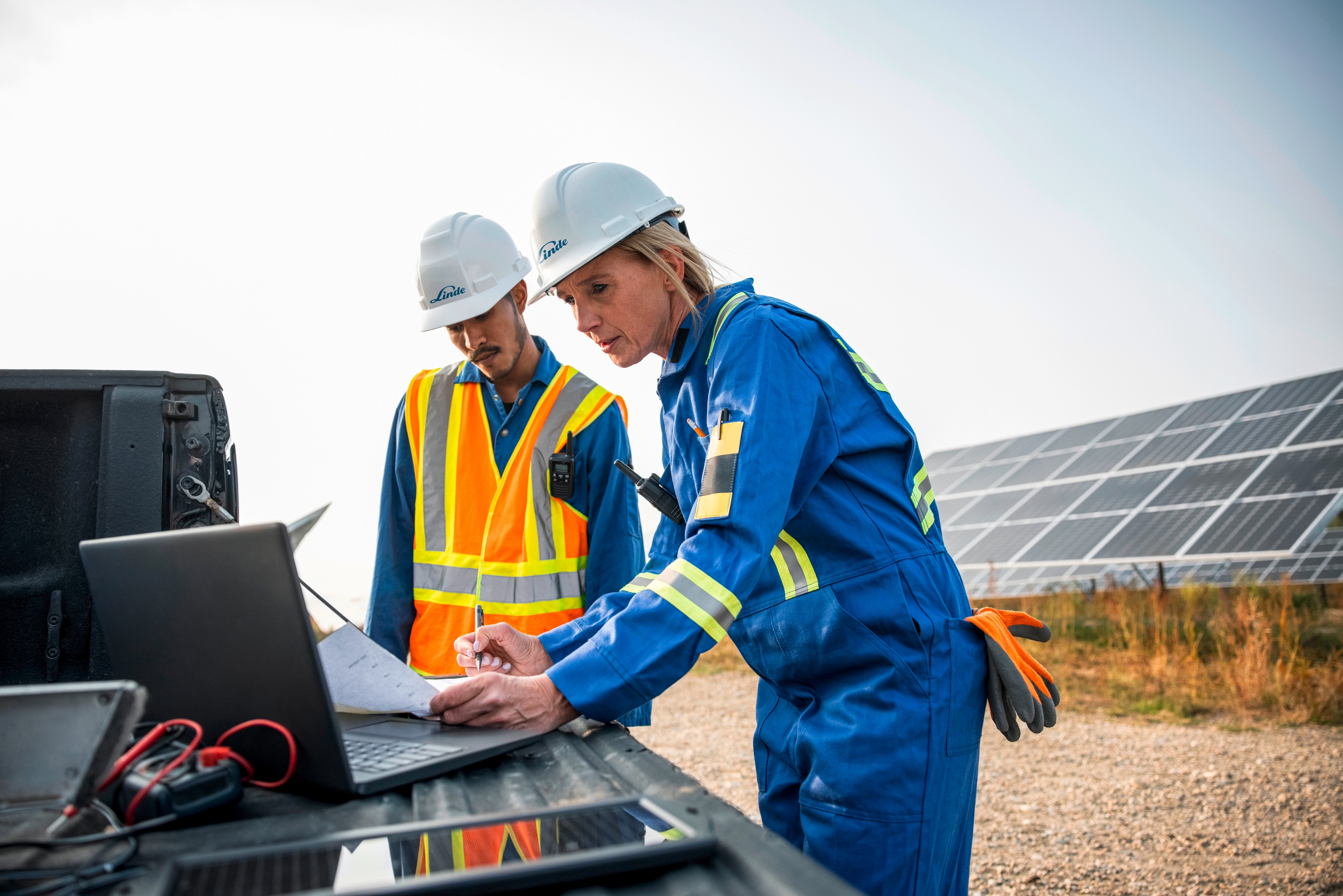Engineers working outside with laptop, solar panels in background
