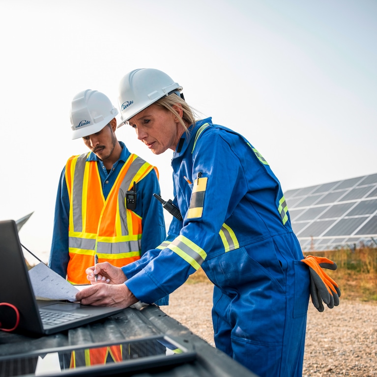 Engineers working outside with laptop, solar panels in background