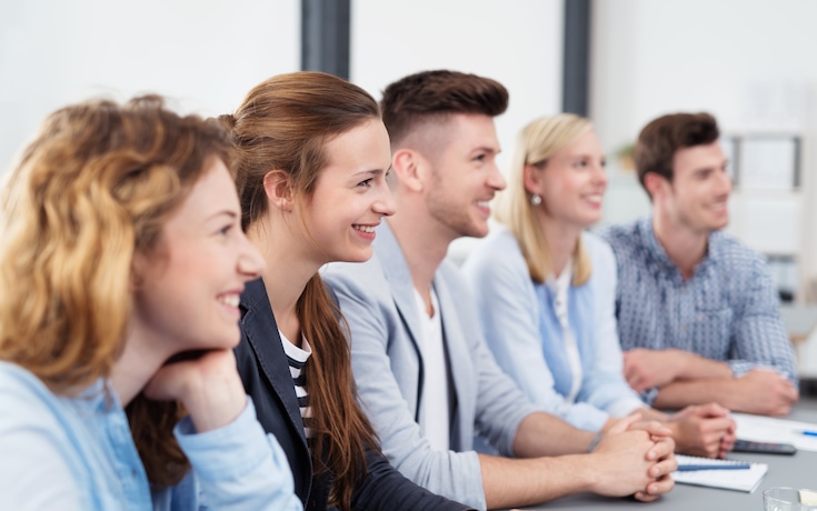 A group of young graduates smiling and listening in a classroom learning environment.