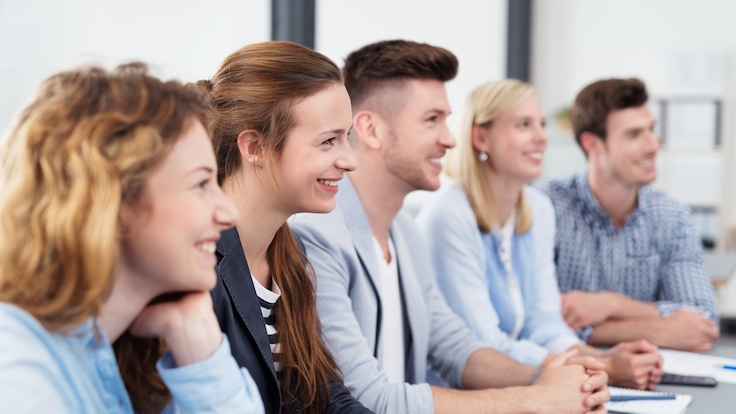 A group of young graduates smiling and listening in a classroom learning environment.