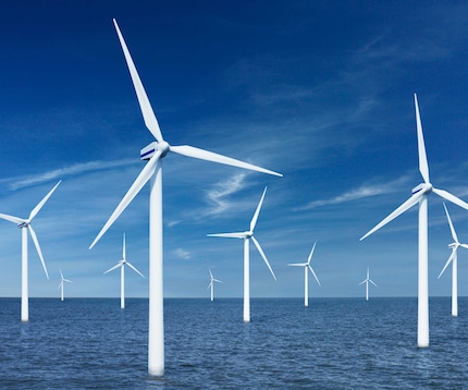 Multiple white offshore wind turbines against a blue sky.