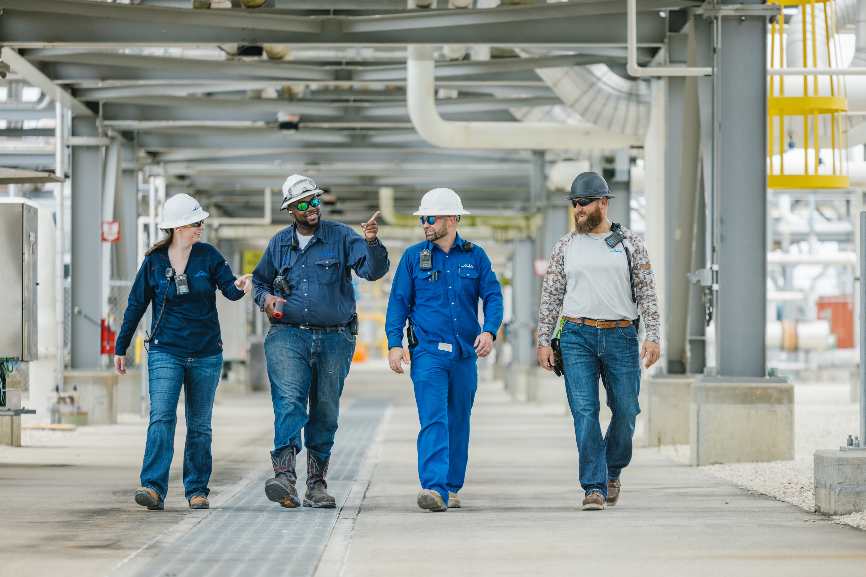 "Four Linde engineers in hard hats talking to each other while walking through an industrial plant."