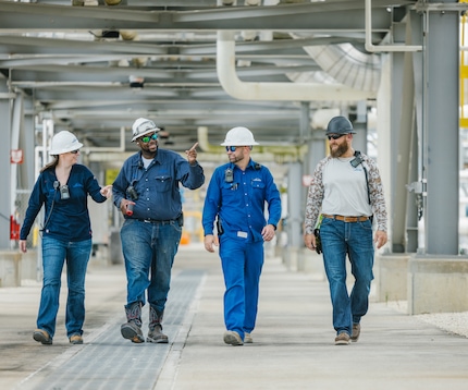 "Four Linde engineers in hard hats talking to each other while walking through an industrial plant."