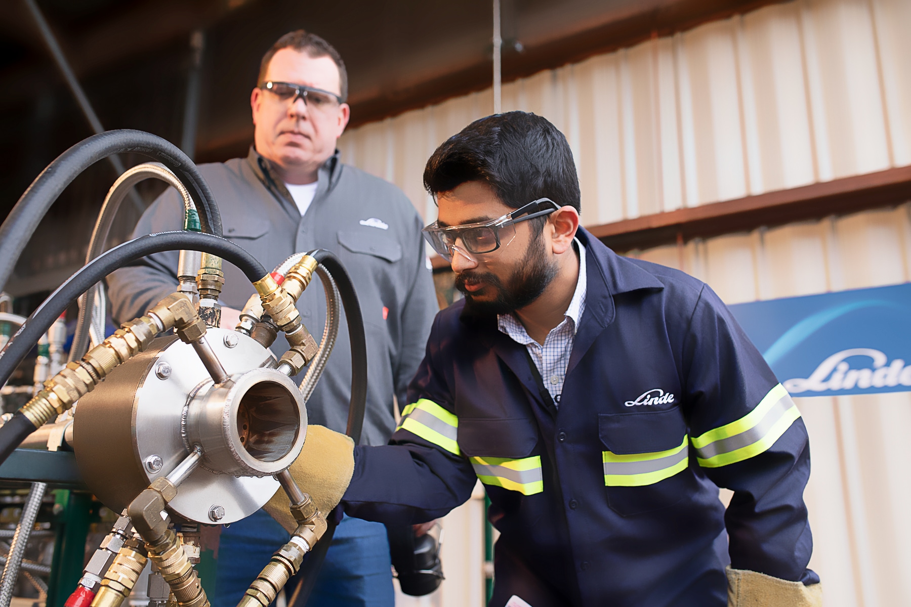 "Two male Linde employees closely inspecting rotating equipment."