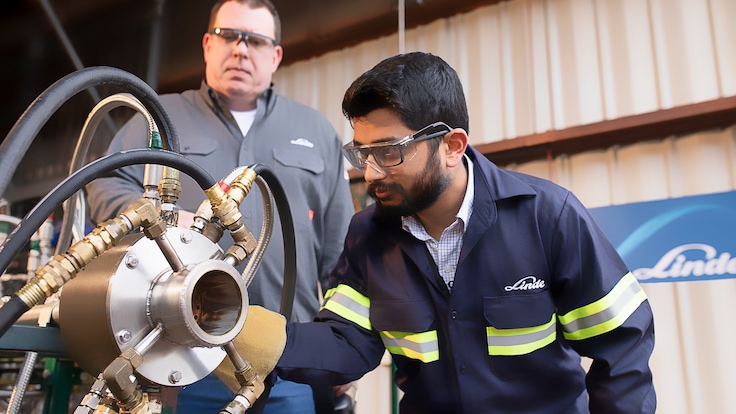 "Two male Linde employees closely inspecting rotating equipment."