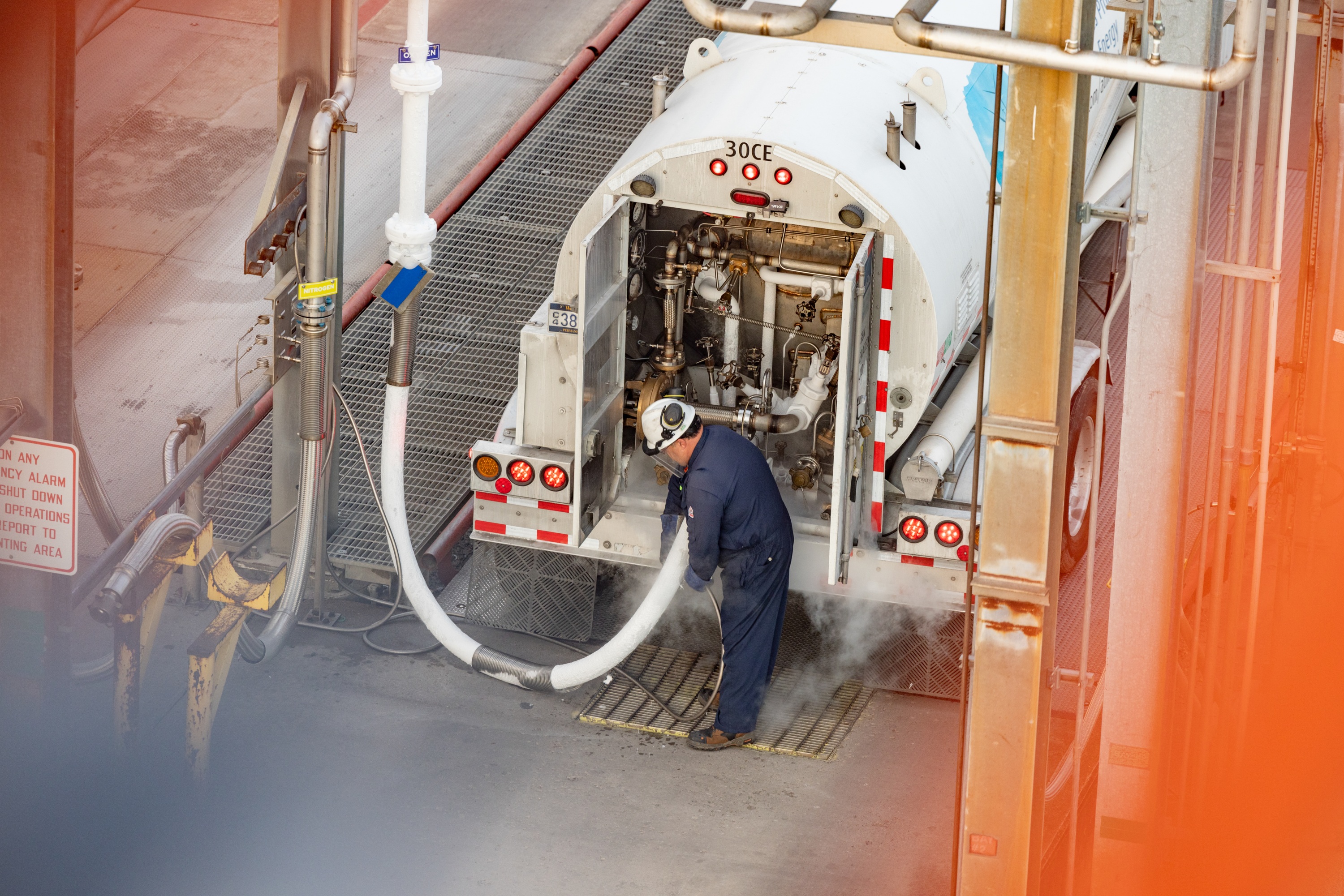 "Aerial view of a driver in personal protective equipment refueling his tanker truck with hydrogen."