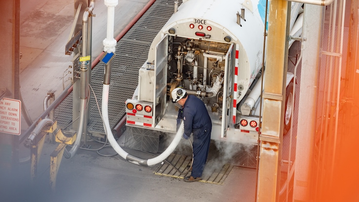 "Aerial view of a driver in personal protective equipment refueling his tanker truck with hydrogen."