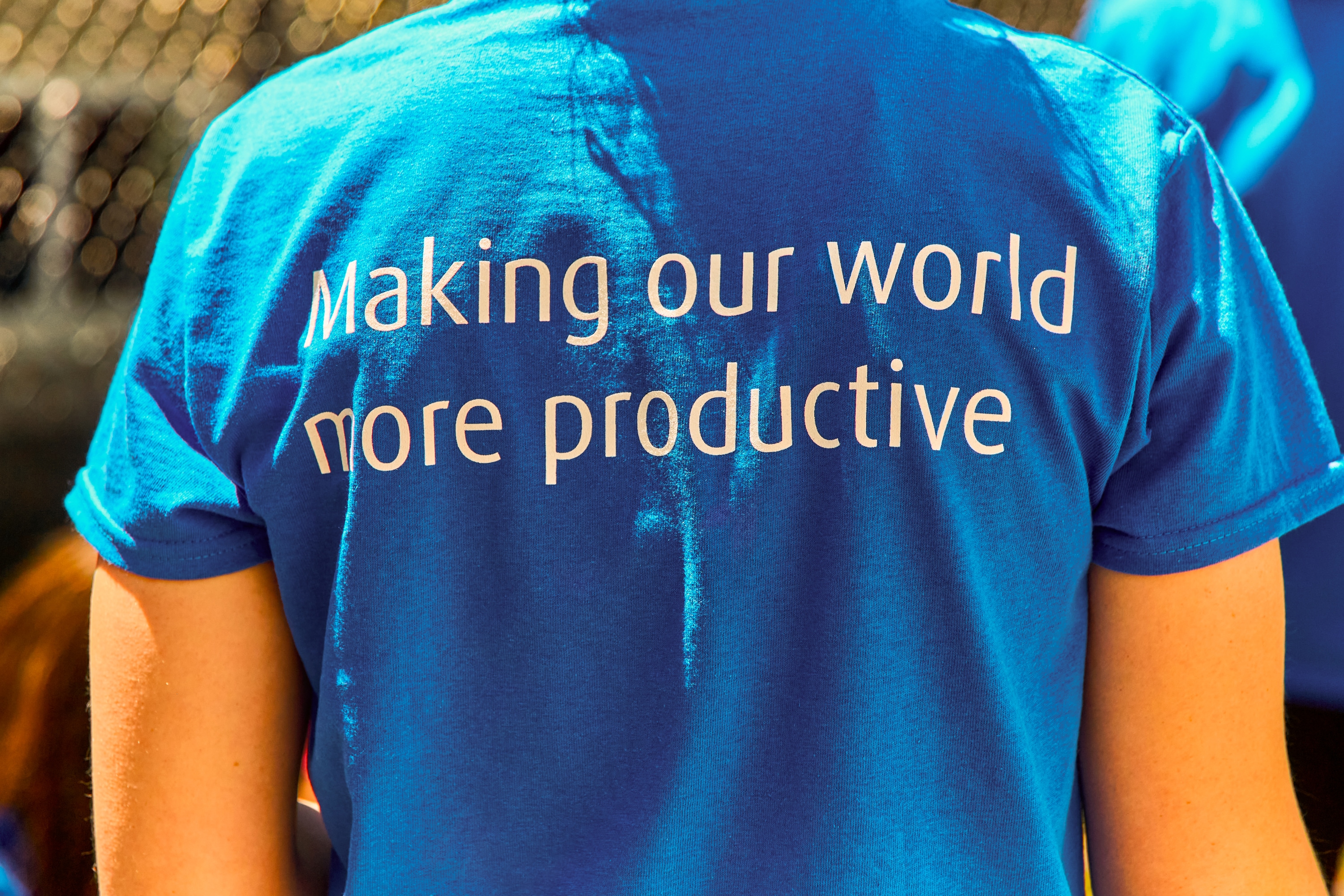 A photograph showing the back of somebody wearing a blue t-shirt with the Linde mission statement “Making our world more productive” written on it. 