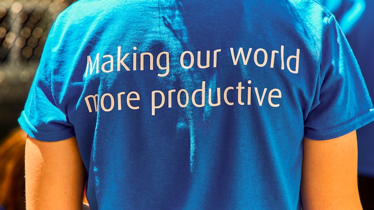A photograph showing the back of somebody wearing a blue t-shirt with the Linde mission statement “Making our world more productive” written on it.