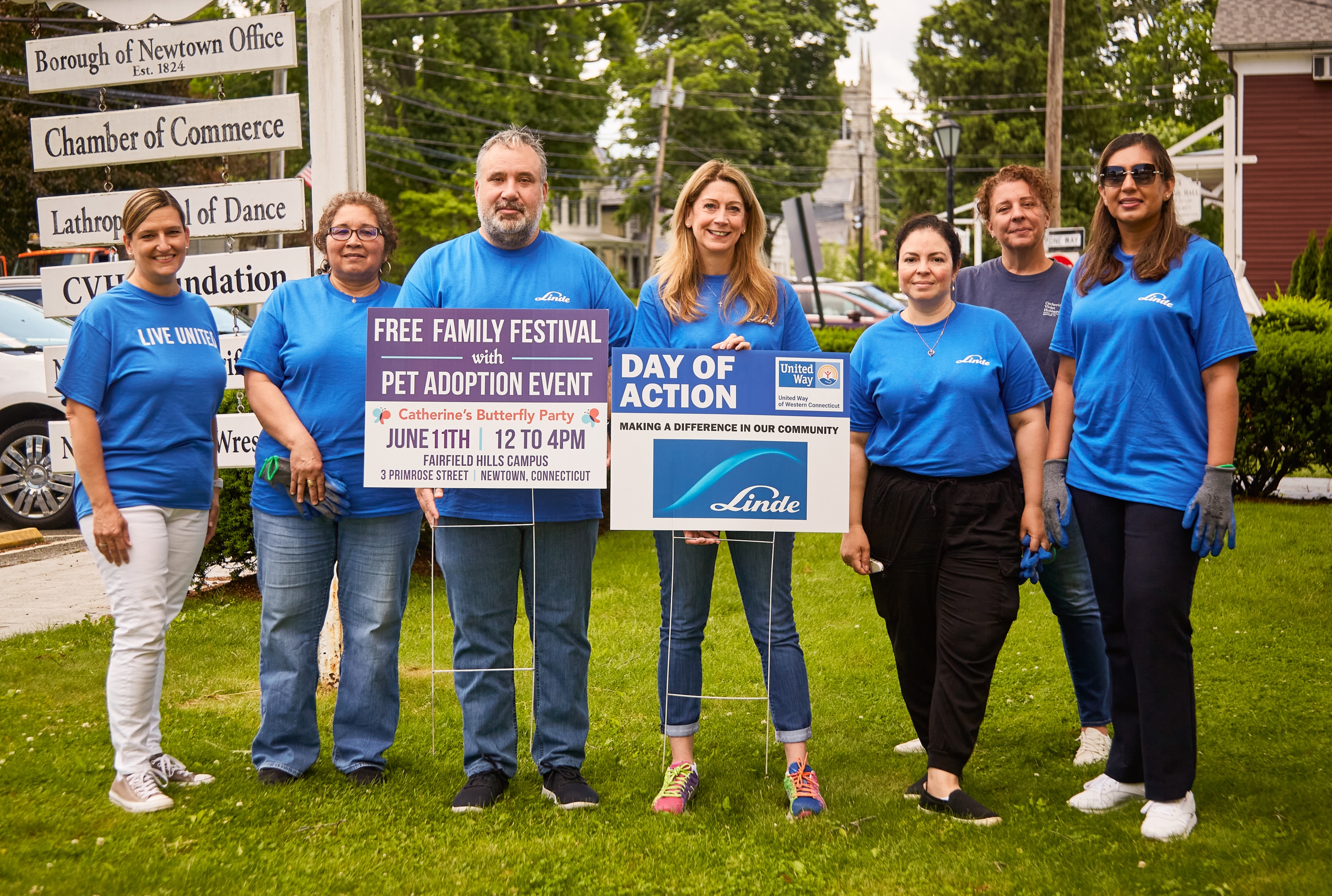 "Group of Linde employees in blue t-shirts at a corporate day of caring event holding signs."