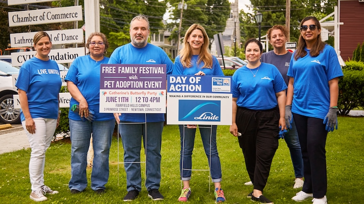"Group of Linde employees in blue t-shirts at a corporate day of caring event holding signs."