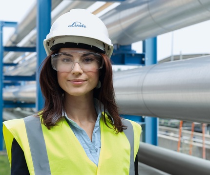 Female businessperson in smart clothes looking directly into the camera with arches of a university courtyard in the background.