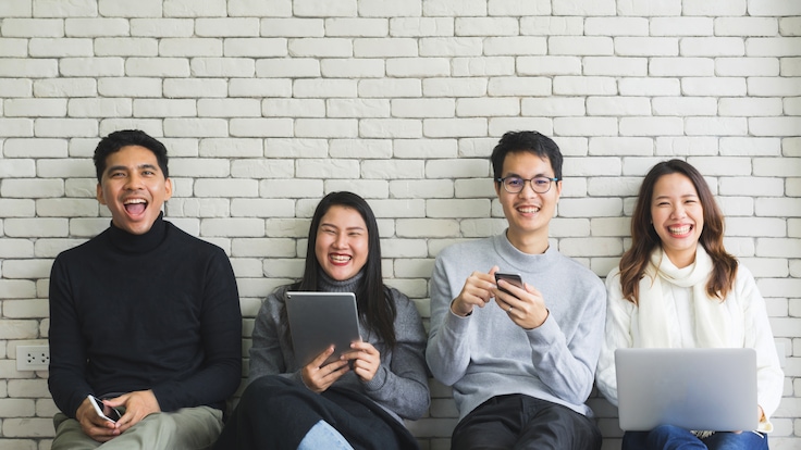 Gruppe junger Leute mit Mobilgeräte vor einer weißen Wand