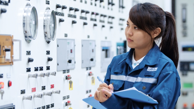 Young apprentice monitors plant controls with clipboard,