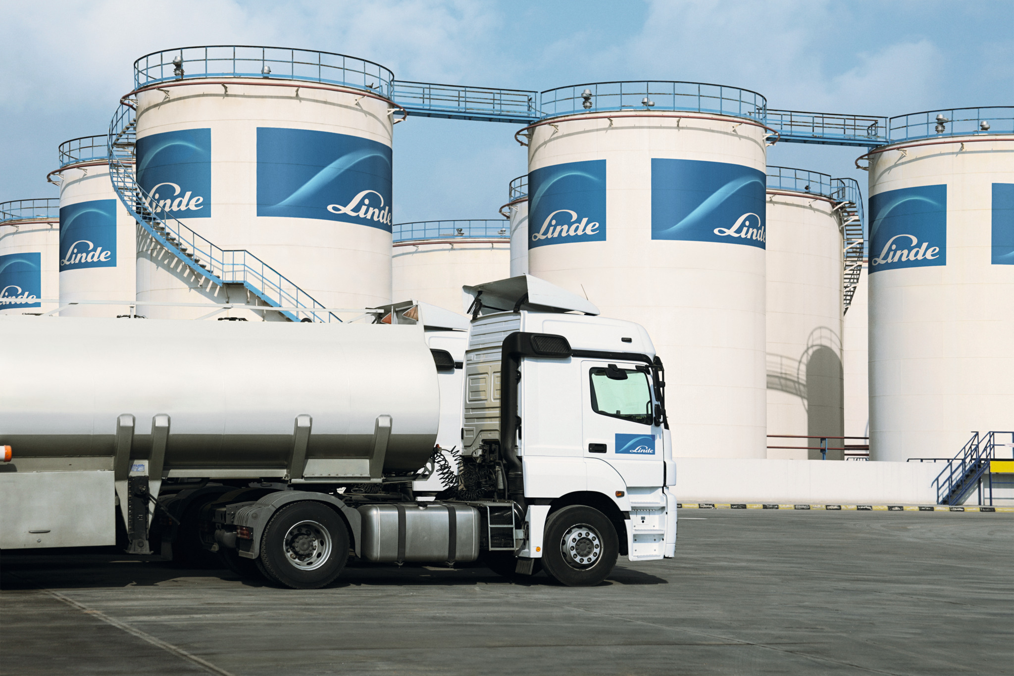 "Frog view of Linde branded tall white hydrogen tanks pointing skyward against a blue sky with clouds."