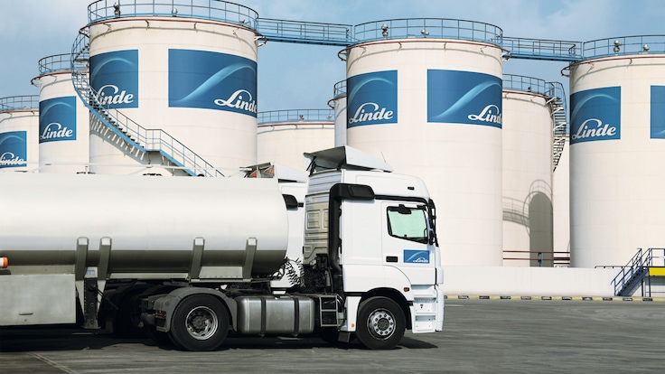 "Frog view of Linde branded tall white hydrogen tanks pointing skyward against a blue sky with clouds."
