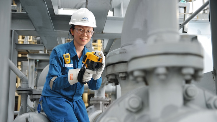 Female businessperson in smart clothes looking directly into the camera with arches of a university courtyard in the background.