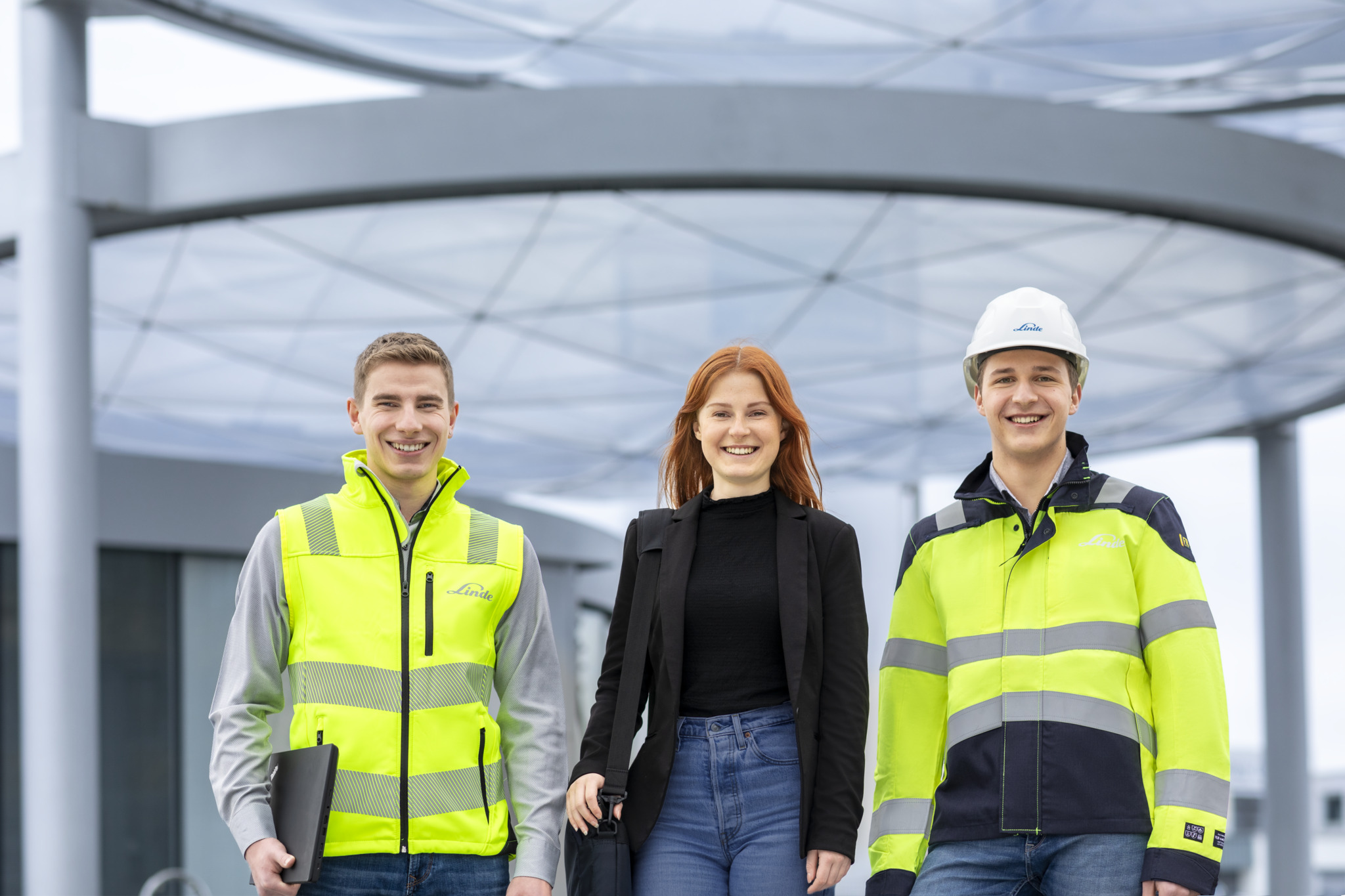 Drei Ingenieure mit Schutzhelmen und Warnwesten stehen vor einem Kraftwerk, mit einem großen, Linde-gekennzeichneten Tank im Hintergrund.