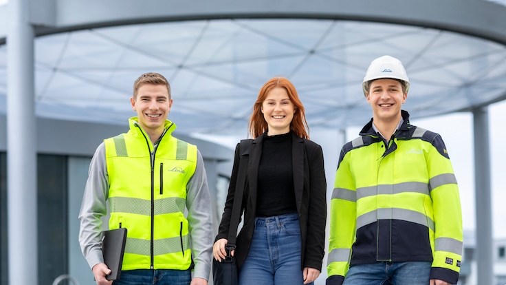 Drei Ingenieure mit Schutzhelmen und Warnwesten stehen vor einem Kraftwerk, mit einem großen, Linde-gekennzeichneten Tank im Hintergrund.