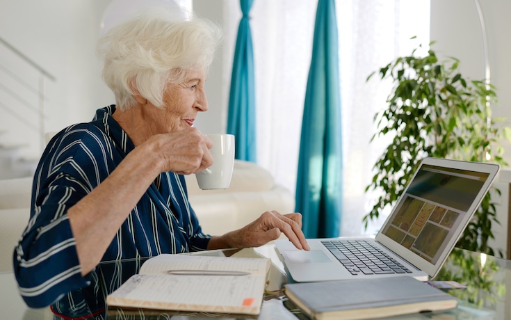 elderly woman drinking coffee while on her laptop