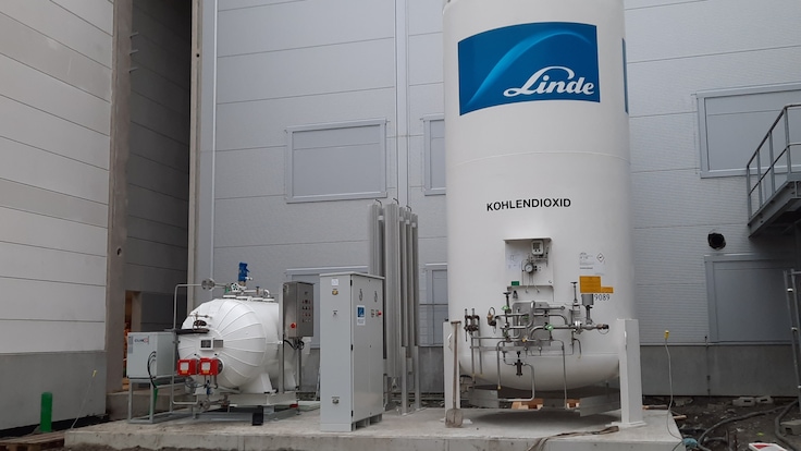 A large Linde branded gas cylinder with piping beside some other industrial equipment.