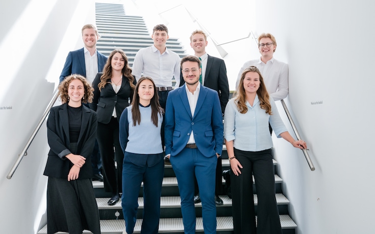 A group of eight young graduates in high visibility vests facing the camera with tall Linde branded gas cylinders in the background.